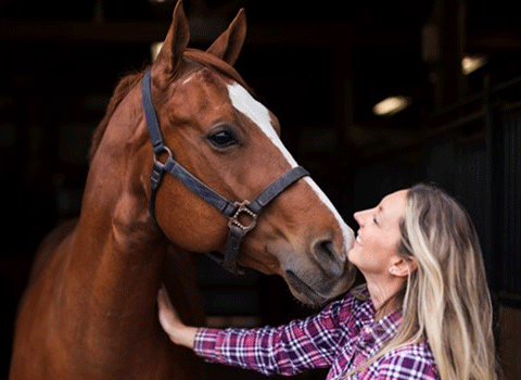 Image of woman standing nose to nose with a brown and white horse